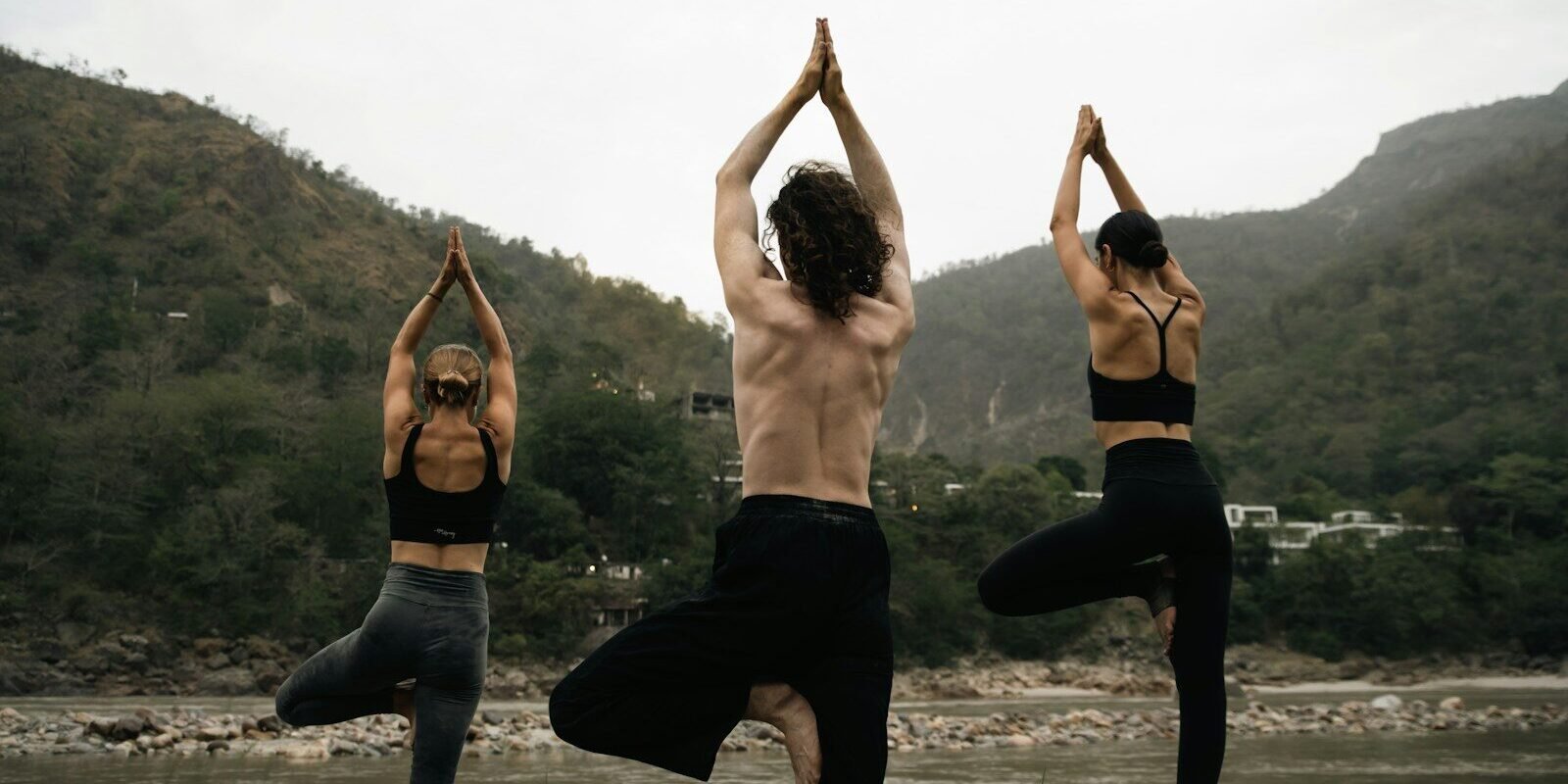 three people doing yoga on a rock near a river